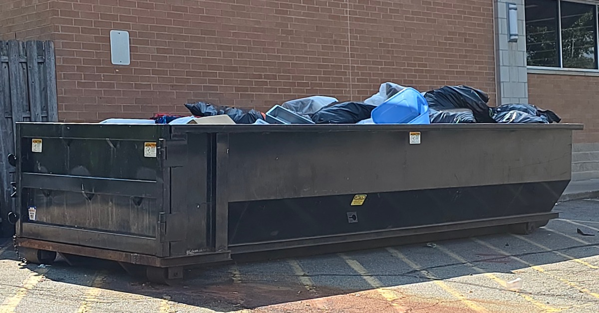A dumpster is sitting in a parking lot next to a building. The dumpster is filled past the brim with garbage.