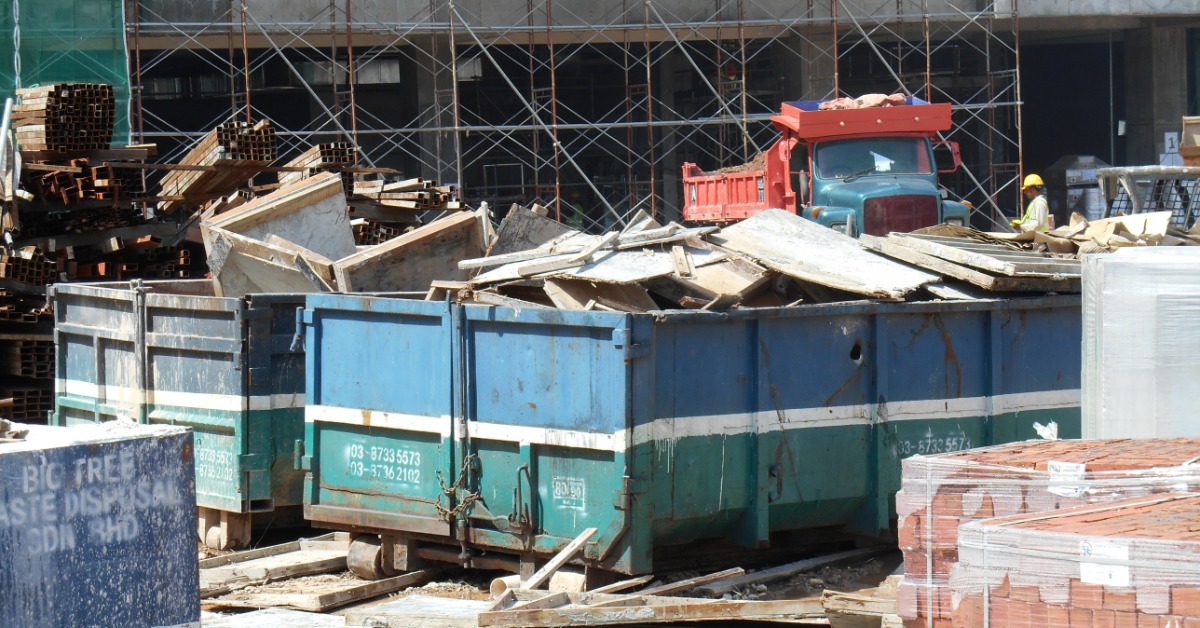 A construction site has two large dumpsters in the middle of it. There is a truck in the background.